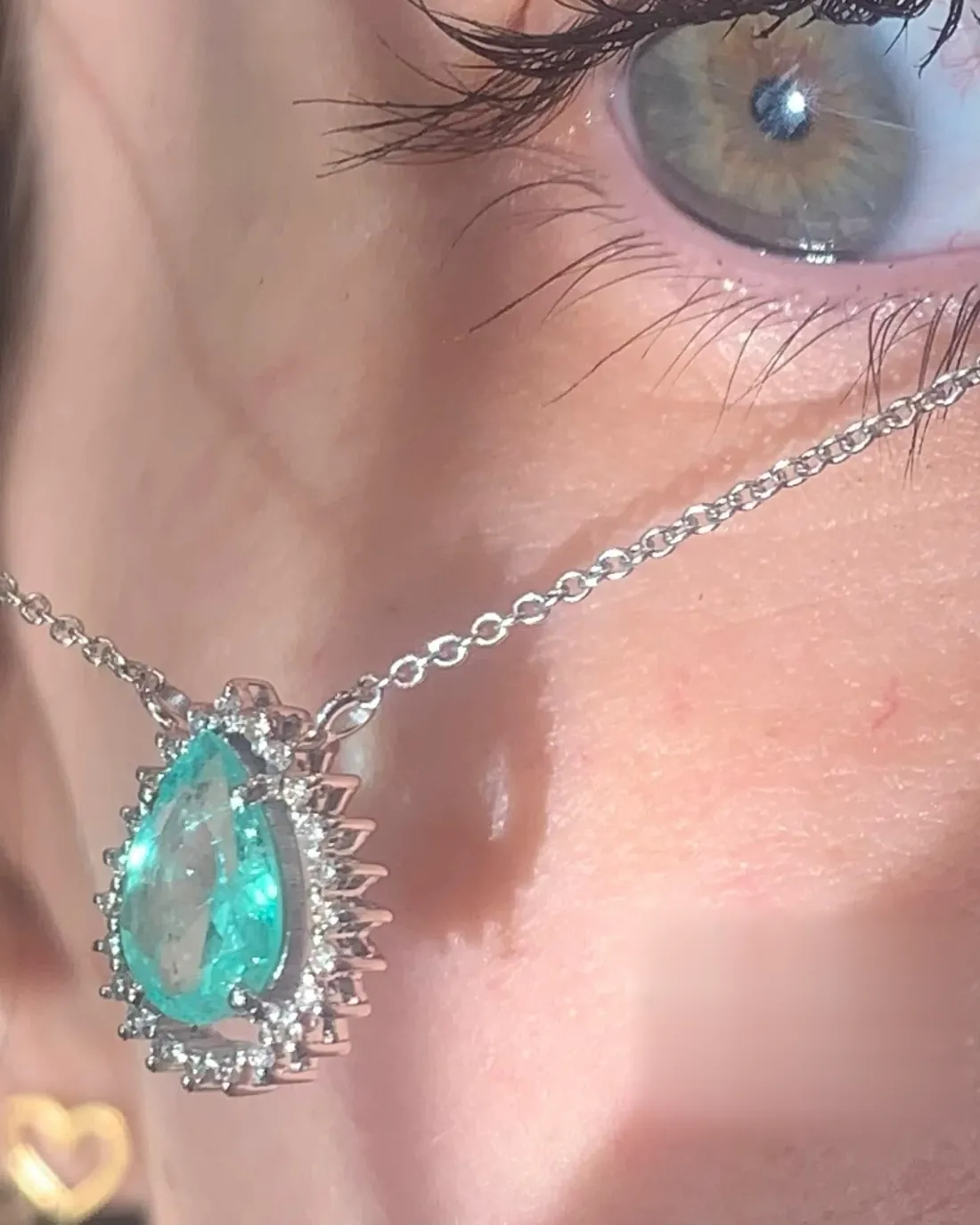 Pingente gota de esmeralda com halo de diamantes usado junto ao rosto